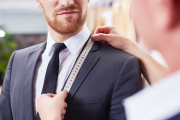 Closeup image of tailor taking measurements of jacket to fit bespoke business suit