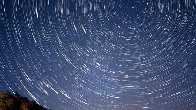 Night sky stars becoming time lapse star trails circling around Polaris the North Star in night sky, shooting star, flight path and northern light flashing by