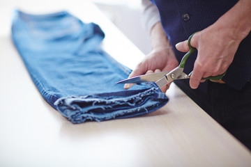 Closeup of man cutting jeans pants on tailors table in atelier