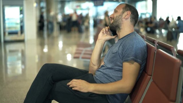 Happy man talking on cellphone while waiting for plane at airport 
