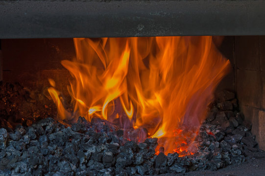Orange flames blaze inside the dark coal forge