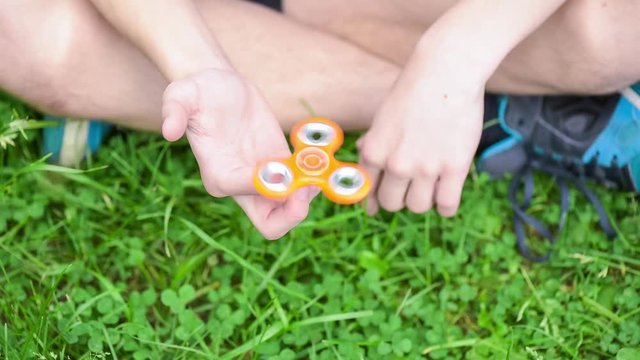 Male child hand holding popular fidget spinner toy - close up, outdoors. Boy playing with a orange Spinner in park.
