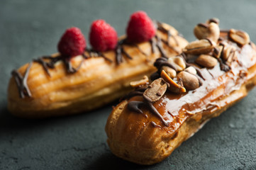 Eclairs with peanuts, chocolate icing and raspberries