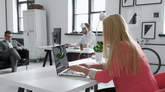 Young business woman working at shared desk in trendy hipster start up office using big data on laptop computer 20s 4k