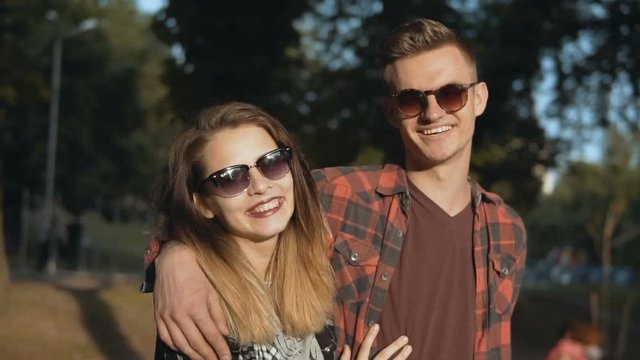 Young attractive couple of teenagers wears sunglasses in park, hipster concept, 120FPS slowmotion