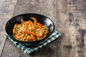 Noodles and shrimps with vegetables in black bowl on wooden table
