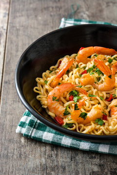 Noodles and shrimps with vegetables in black bowl on wooden table
