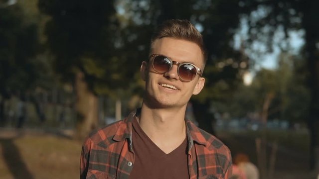 Portrait of young attractive sexy blond man wears sunglasses in park, hipster concept, 120FPS slowmotion