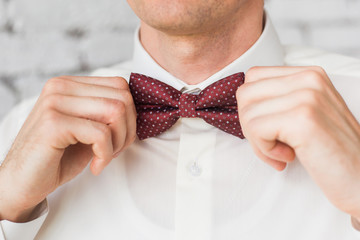 Closeup of adult handsome man adjusting stylish brown male bow tie while preparing for formal event. Anonymous elegant groom getting ready for wedding ceremony. Horizontal color photography.