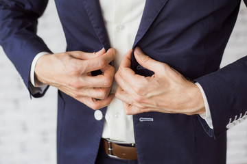 Handsome stylish man dressed in modern formal clothes buttoning jacket. Close up of hands of guy in blue jacket, white shirt. Person ready for wedding celebration, graduation or business meeting.