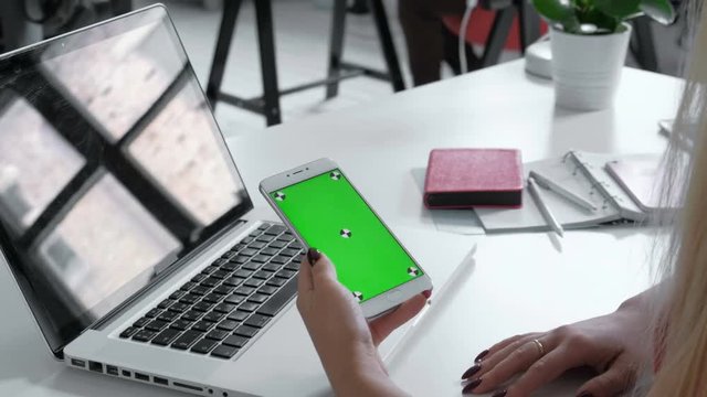 Hands top view. Woman using her smartphone with green screen in table , scrolling news, photos. Office desk background. 20s 4k