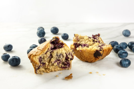 Two halves of blueberry muffin with fresh blueberries