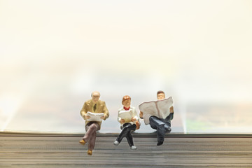 Reading and hobby concept. Group of miniature mini figures businessman and woman sitting on a book...