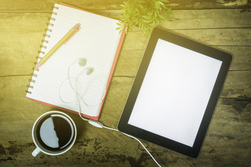tablet with blank screen and a cup of coffee ear phone flower pot on the desk in coffee shop cafe,an office tablet with blank white screen ready for content text ,vintage tone,selective focus.