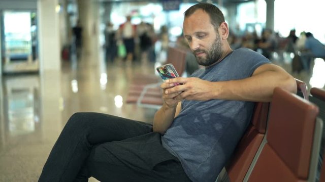 Young man texting on smartphone while waiting for plane at airport 
