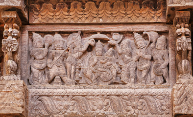 Servants and admirers of the Indian god on carved wooden wall of traditional Hindu temple. Ancient artwork of old religious structure in India