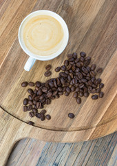Cup of espresso coffee and coffee beans on rustic wood board.