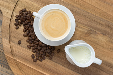 Coffee concept: Top view of  white porcelain cup filled with delicious frothy coffee, jug of milk...