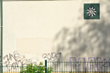 Mauer mit Zaun davor, Lüfter und Graffiti