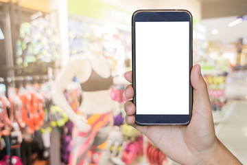 hand holding mobile smart phone , tablet,cellphone over blurred background of woman buys in the store swimsuit. beautiful young woman chooses clothes in shop,boutique sale women underwear clothes