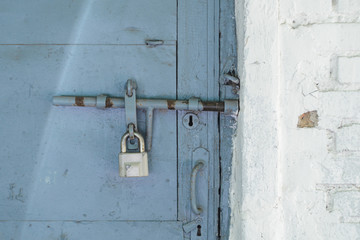 Padlock on the blue metal door. Locked on the castle is an old door in a white brick wall. Abstract background