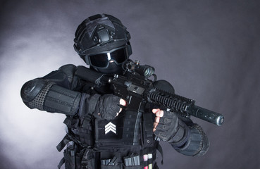 Member of the SWAT squad with an assault rifle in a black uniform on dark background. Special...
