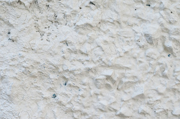 Old white concrete wall with many protruding stones