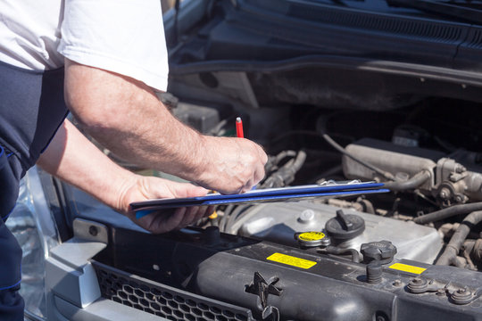 Car or auto mechanic checking a car engine and writing on the clipboard