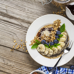 Healthy breakfast trend. Thin oat pancakes with banana, blueberries, goji berries, sesame and chia seeds with chocolate cream and fresh cream portions served with honey, mint and peanuts