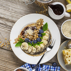 Healthy breakfast trend. Thin oat pancakes with banana, blueberries, goji berries, sesame and chia seeds with chocolate cream and fresh cream portions served with honey, mint and peanuts