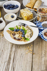 Healthy breakfast trend. Thin oat pancakes with banana, blueberries, goji berries, sesame and chia seeds with chocolate cream and fresh cream portions served with honey, mint and peanuts