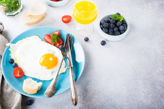 Fried egg on blue plate, tomatoes, blueberries, mint tea and orange juice. Healthy breakfast concept with copy space.