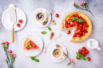 Overhead shot of cups of coffee, delicious homemade strawberry cheesecake and flowers on light gray background. Top view, flat lay.