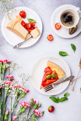 Overhead shot of cups of coffee, delicious homemade strawberry cheesecake and flowers on light gray background. Top view, flat lay.