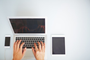 High angle view of technology composition, male hands typing on laptop keyboard, tablet and smartphones placed near portable computer