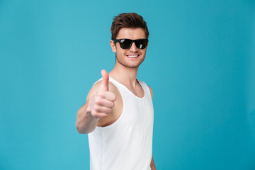 Smiling young guy in sunglasses showing thumbs up