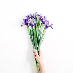 Female hand holding beautiful purple iris flowers bouquet on white background. Flat lay, top view.