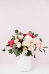 Beautiful flowers bouquet: bombastic roses, blue eringium, eucalyptus branches in flowerpot at pale pastel pink wall. Floral lifestyle composition.