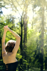 Carefree girl with raised hands stands on the nature background on sunny summer day