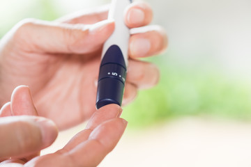 Medicine, diabetes, glycemia, health care and people concept - close up of man hands using lancet on finger to check blood sugar level by Glucose meter