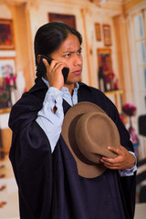 Close up portrait of young indigenous man wearing hat and poncho using cell phone