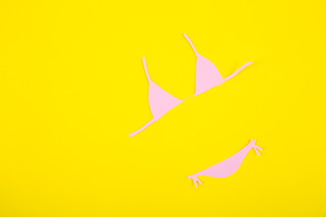 Pink paper bikini swimsuit on yellow background. Minimalistic summer flat lay.