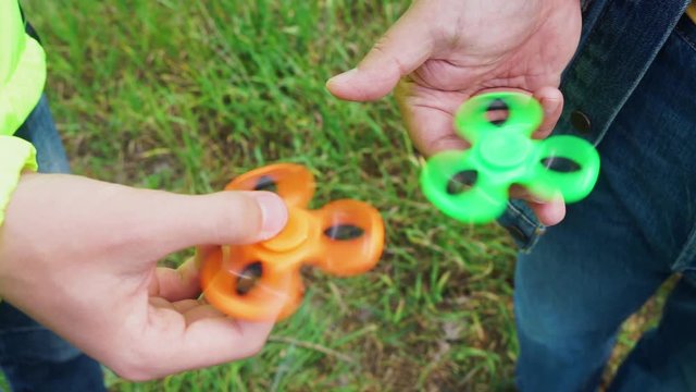 trendy fidget spinner - two persons holding spinning green and orange fidget spinners in hands, close up view