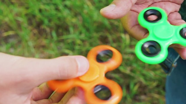 trendy fidget spinner - two persons holding spinning green and orange fidget spinners in hands