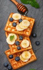 Traditional Belgian waffles with blueberries, banana and honey on a black slate plate. Gourmet Breakfast. Selective focus