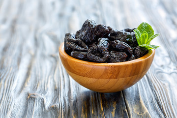 Dried black plums in a wooden bowl.