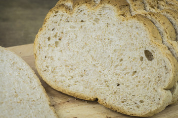 wholegrain rye bread with seeds on a weathered wooden board, rustic earthenware in the dark background