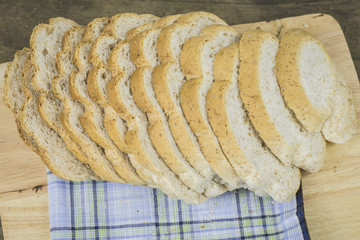 wholegrain rye bread with seeds on a weathered wooden board, rustic earthenware in the dark background