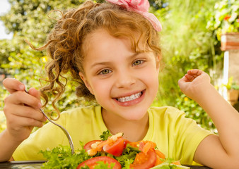 Close up of a smiling beautiful girl, wearing a yellow t-shirt preparing to eat a healthy salad with a fork, in a garden background