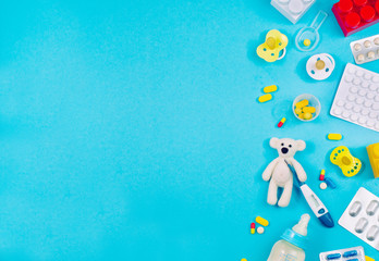 Assorted pills and bear toy with electronic thermometer on blue backround